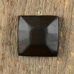 A pyramid hammered square head bolt that is painted black with a rusty metal patina installed on a wood background.