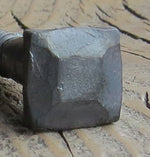 A side view of a pyramid hammered square head bolt that has a wrought iron finish on a wood background. 