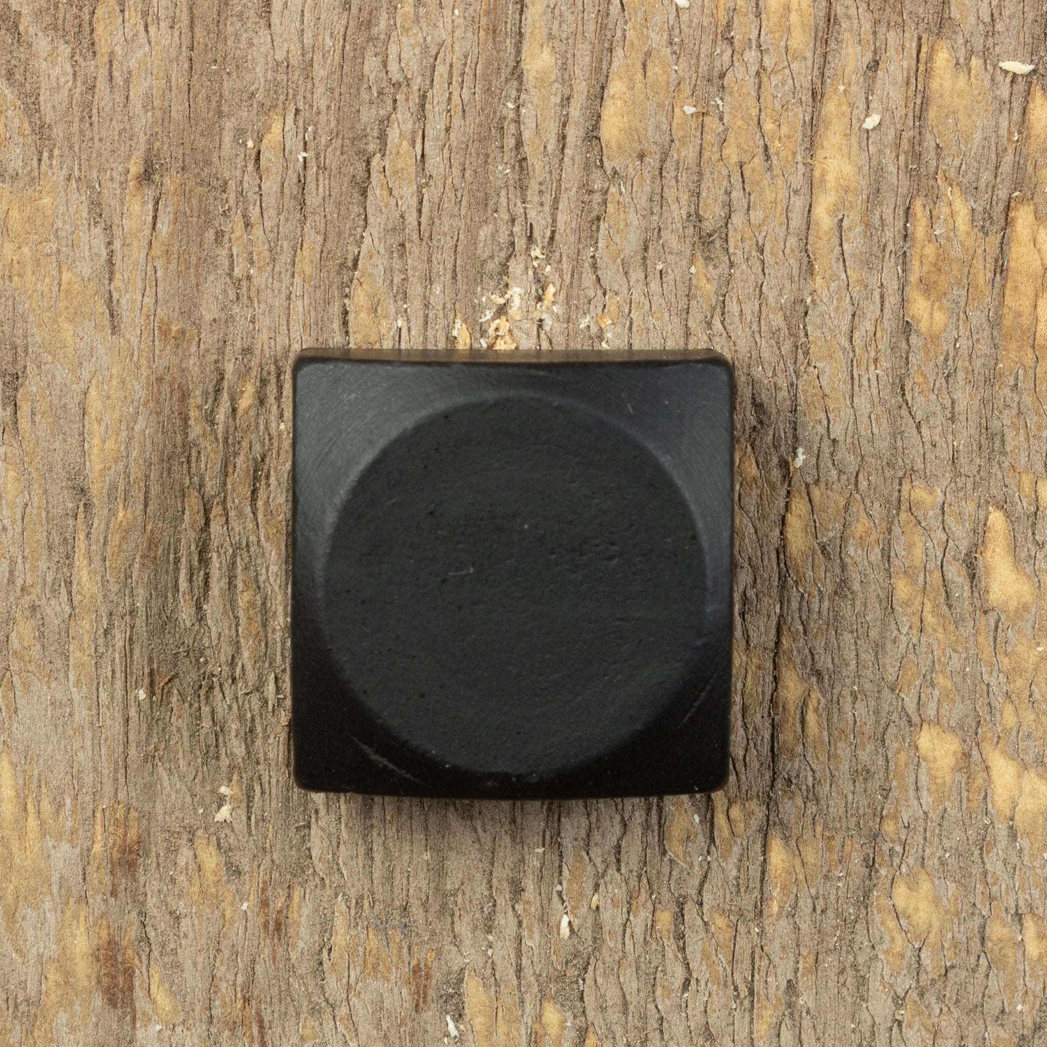 A square head bolt with a smooth texture and painted black on a wood background.
