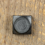 A top view of a square head lag with a smooth texture painted black with an aged pewter patina finish screwed into a wood background.