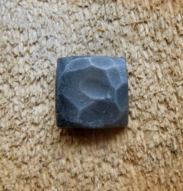 A top view of a hand hammered square head lag that has been painted black with an aged pewter patina finish screwed into a piece of wood as the background.