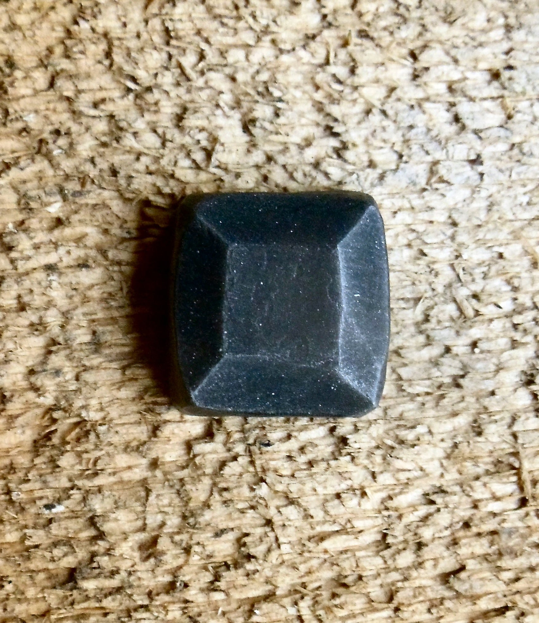 A top view of 3/4in hand hammered pyramid square head lag that is painted black with a pewter patina installed on a wood background.