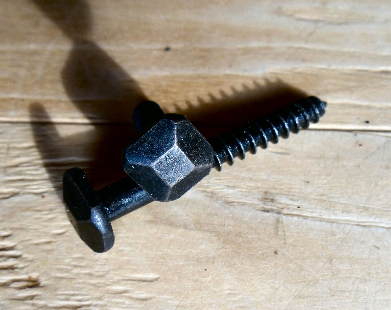 A black square pyramid head decorative screw on a wooden surface.