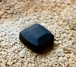 A square head bolt that has been pyramid hammered and painted black installed on a wood background. 