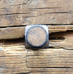  Smooth textured square head bolt painted black and finished with an aged bronze patina installed on a wood background. 