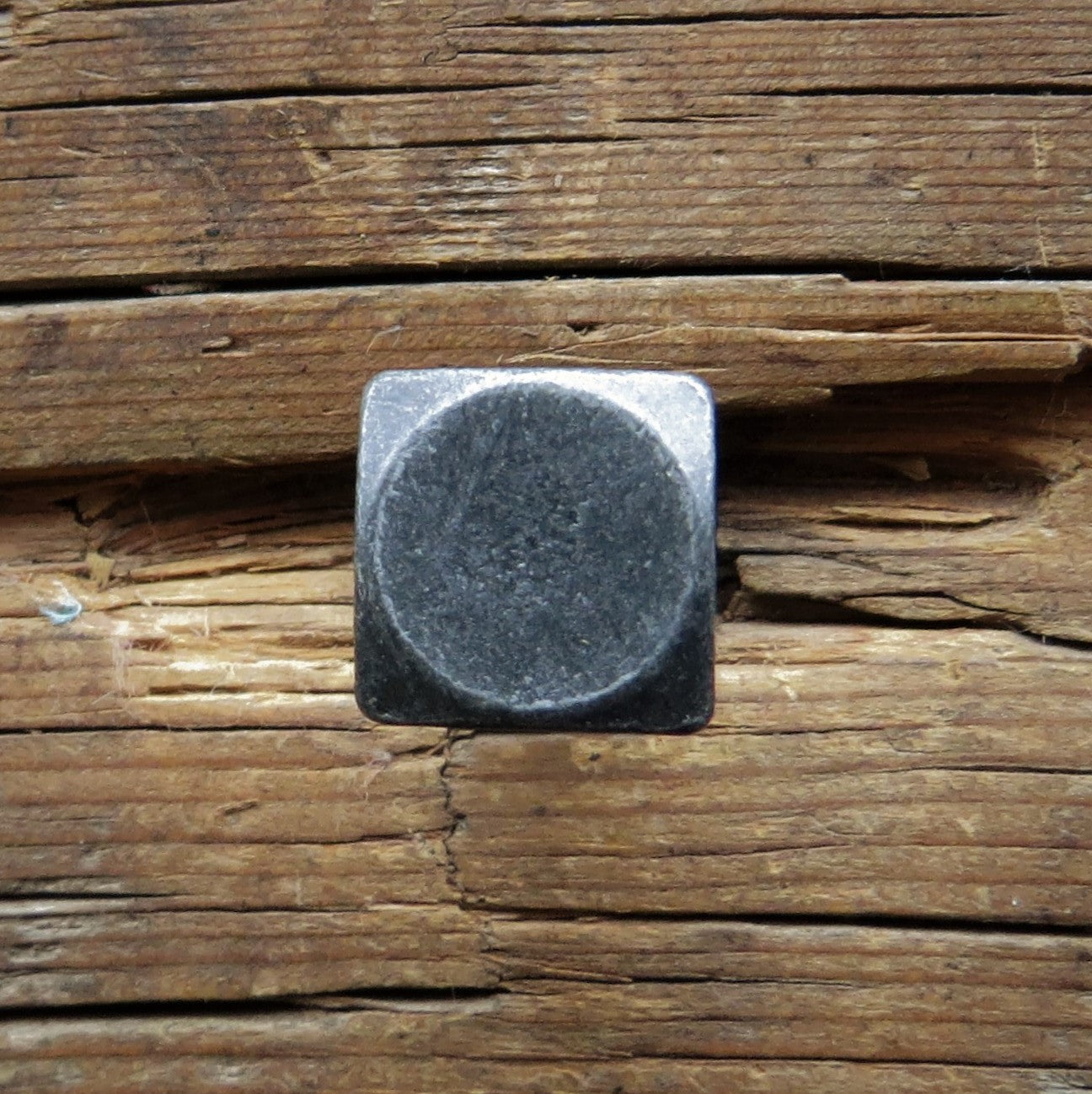 A square head bolt with a smooth texture painted black finished with a pewter patina installed on a wood background.